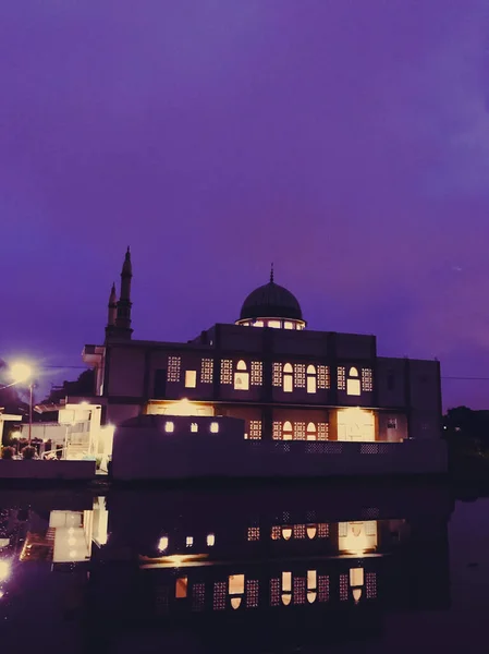 Gece, dramatik bir mor gökyüzünün altında aydınlanan güzel bir cami ön plandaki sakin suya açıkça yansıyor..