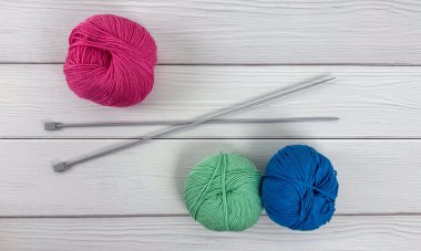 Üzerinde çapraz metal örgü iğneleri olan pembe iplik topu ve nane ve mavi renkli iki iplik yumağı beyaz ahşap masada. Kopya alanı ile temiz düz konum, örgü desenleri, kılavuzlar ve el sanatları afişleri için uygun