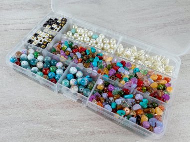 İnciler, alfabe boncukları ve renkli değerli boncuklar da dahil olmak üzere karışık mücevher üreten açık plastik organizatör. Hafif ahşap arka plandaki bölmelere yerleştirilmiş el işleri malzemeleri..