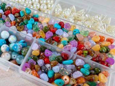 Renkli boncuklar ve inci boncuklar eşliğinde plastik organizatörlerde sıralanmış çeşitli takı boncuklarının makro yakın çekimi. Tasarım ve boncuklama malzeme dokusu arka planı.