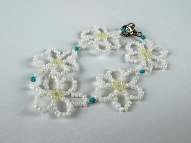 Beyaz çiçek şekilli el yapımı boncuklu bilezik ve soluk sarı merkezler, küçük turkuaz boncuklar ve metal tokayla bağlanmış. Mücevher dairesi temiz ışık zemininde yatıyordu.