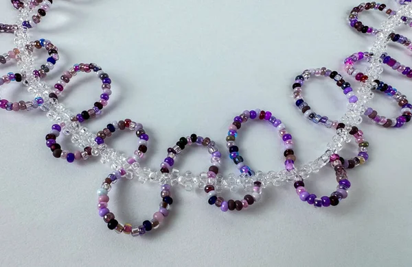 Temiz kristal boncuk zincirine bağlı mor tohum boncuk halkaları ile el yapımı mücevherler. Açık gri zemin üzerinde geniş kopya alanı olan çapraz sınır kompozisyonu. Mücevher tasarımı, el yapımı zanaat ve afiş tasarımları için uygun