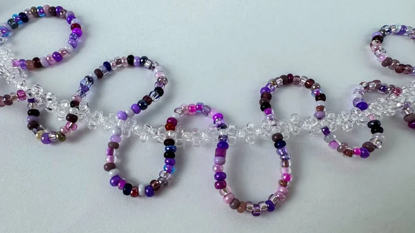 Temiz kristal boncuk zincirine bağlı el yapımı mor boncuk halkalarını kapatın. Açık gri arkaplan üzerinde minimum düz yatıyordu metin için kopyalama alanı ile. El işi, mücevher yapımı ve soyut geçmiş kavramları için ideal.