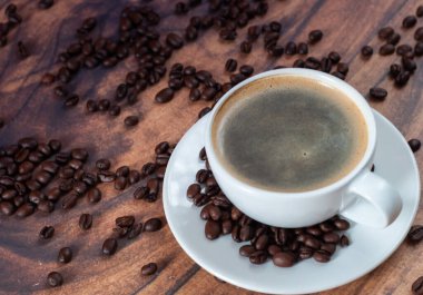 Bir fincan sade kahve ahşap bir masanın üzerinde duruyor. Masa kahve çekirdekleri ile kaplı, rahat ve misafirperver bir ortam yaratıyor. Sıcaklık ve rahatlık kavramı