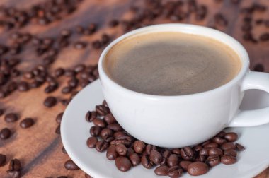 Beyaz kahve fincanı, etrafında kahve çekirdekleri olan bir ahşap masanın üzerinde duruyor..