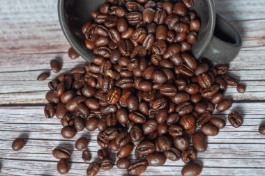 Bir fincan kahve çekirdeği ahşap bir masanın üzerine dökülür. Fasulyeler masanın her tarafına saçılmış.