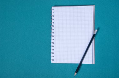 Bir kalem ve spiral kaplı bir defter mavi bir yüzeye oturur. Defter boş ve kalem sivri uçlu. Sahne bir anlık tefekkür ya da yazma hazırlığı öneriyor.