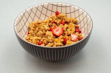 Çilekli ve kuru üzümlü bir kase mısır gevreği. Kasede beyaz ve gri çizgili desenler var.