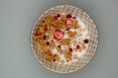 Bir kase mısır gevreği, çilek ve granola. Kâse beyaz ve ızgara deseni var.