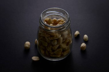 Fıstıklı cam kavanoz, karanlık bir yüzeye yerleştirilmiş. Doğal yaşam tarzı görselleri ve diyet kavramları için sağlıklı atıştırmalıklar ve vejetaryen gıda fikri.