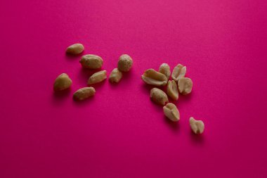 Bir avuç kavrulmuş fıstık stüdyonun ışığı altında parlak pembe arka plana saçılmış. Basit kompozisyonda sağlıklı atıştırmalıklar ve canlı bir kontrast vurgulanıyor..