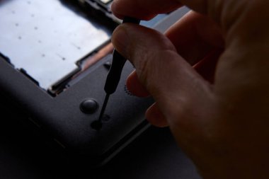 Bir dizüstü bilgisayarın arka panelini tamir etmek için tornavida kullanan birinin yakın çekimi. Görüntü, el işi, modern teknoloji ve bilgisayar bakım araçlarını gösteriyor..