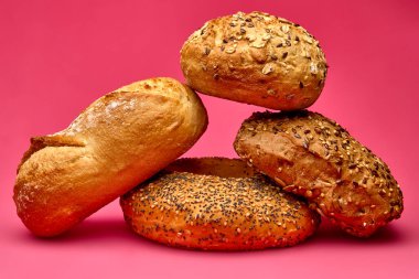 Artistic composition of three assorted bread rolls on pink background photographed in studio light. Conceptual still life suitable for bakery advertising or editorial design.