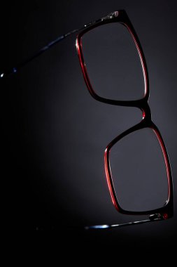 Kırmızı çerçeveli gözlüklü, koyu renk arkaplanlı gözlüklü stüdyo. Moda aksesuar ve vizyon bakım ürünlerini temsil eden kavramsal görüntü.