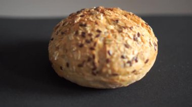 Koyu arkaplanda çekilen çeşitli tohumlarla kepekli ekmek rulosu. Pastane konsepti için kabuk dokusu ve yemek detaylarını gösteren makro video döngüsü.
