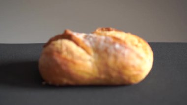 Koyu tarafsız zemin üzerine altın kabuklu taze pişmiş beyaz ekmek. Kamera pürüzsüz döngü hareketinde kabuk dokusunun detaylarını düzgünce gösterir.