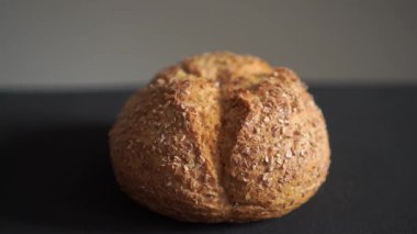 Kırsal yuvarlak ekmek rulosu. Kabukta derin çatlak var. Koyu arkaplanda yakın plan çekiliyor. Zanaatkar fırın ürünü dokusunu ve altın fırınlanmış yüzeyi gösteren kusursuz bir video döngüsü..