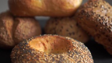 Karanlık yüzeyde haşhaş tohumlu simit stüdyosunu kapat. Fırın ve gıda konsepti için fırın kabuğu dokusunu ve karamsar ışıklandırmayı gösteren döngü videosu.