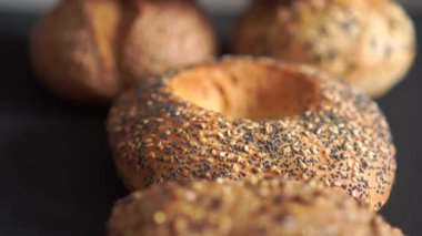 Macro stüdyosunun karanlık arka plana yerleştirilmiş haşhaş tohumu simitlerinin videosu. Kabuk dokusunu, fırınlanmış yüzeyi ve zanaatkar gıda kavramını vurgulayan döngü görüntüleri.
