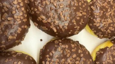 Üst görüntüde, üzerinde fındık parçaları olan çikolatalı çörekler var. Videoda taze pişmiş tatlıların simetrisi, dokusu ve ılık tonları vurgulanıyor.