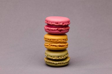 Gri arkaplanda pembe, sarı ve yeşil desenli üç renkli badem kurabiyesi yığını. Modern estetik stüdyoda yemek fotoğrafçılığı.
