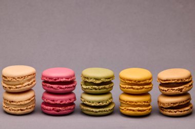 Gri yüzeydeki sıralı yığına yerleştirilmiş beş renkli badem kurabiyesi seti. Ticari kullanım için dengeli ve şık stüdyo tatlı imajı.