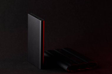 SSD sürücüsünün, koyu yüzeye yansıyan kırmızı ışıkla aydınlatılmış bir stüdyo fotoğrafı. Minimalist teknoloji modern donanım estetiği ve hız kavramını gözler önüne seriyor..