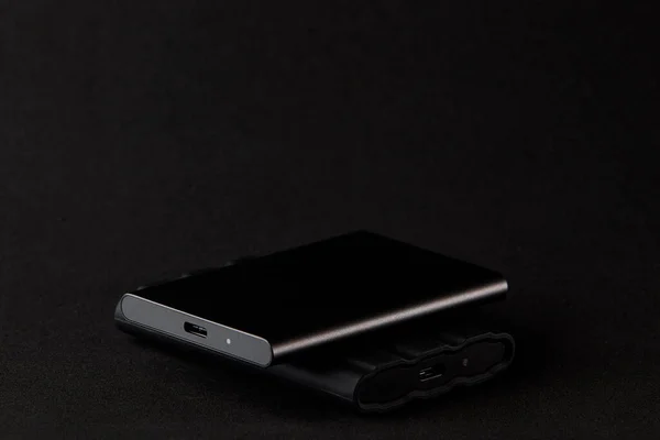 Siyah arkaplandaki güç bankasına bağlı taşınabilir SSD fotoğrafı. Mobil iş ve hızlı veri transferi için kullanılan modern teknoloji aksesuarlarını gösteren minimalist natüralist.