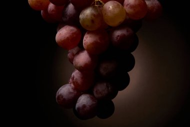 Kırmızı üzümlerin yakın plan koyu bir arkaplana hafifçe yayılmış ışıkla aydınlatılması. Resim stüdyosunun yemek fotoğrafçılığı doku ve renk detaylarını gösteriyor.