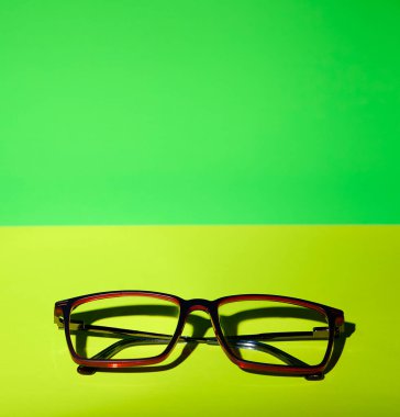 Yeşil ve sarı arkaplana yerleştirilmiş bir gözlük. Sahte güneş ışığıyla çekilmiş. Kompozisyon, reklam veya tasarım kullanımı için temiz, minimal ve mükemmeldir.