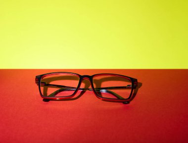 Stüdyoda yaratıcı ışık altında çekilmiş sarı ve kırmızı bir yüzeye yerleştirilmiş gözlük. Sıcak tonlar ürün pazarlaması için ticari açıdan hazır görsel bir ideal oluşturuyor..