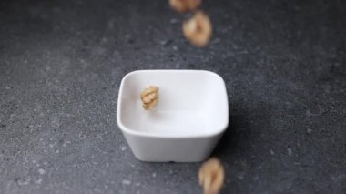 Macro, fındıkların yakın plan gri desenli arka planda küçük beyaz bir kaseye düşüşü. Fındık detaylarını gösteren doğal gıda kavramı ve metin veya tasarım için kopyalama alanı ile dinamik düşme hareketi.