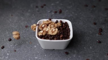 Kahve çekirdekleri ile dolu beyaz bir seramik kaseye düşen ağır çekim makro ceviz. Doku ve tonların karışımı yiyecek ve içecek kavramları için uygun en az bileşimi oluşturur..