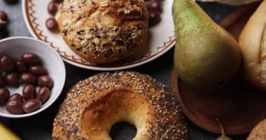 Kırsal bir kompozisyonda, armutlar, muzlar ve çikolatayla tamamlanmış ahşap bir tabakta sanatsal fırın çörekleri yer alır. Pürüzsüz sürgülü hareket ve yumuşak ışık yiyecek medyası için rahat ve iştah açıcı bir hayat yaratır.