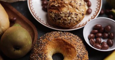 Rafine bir masa üstü sahnesinde ahşap bir tabakta altın çörekler, armutlar, muzlar ve çikolatalı fındıklar gösteriliyor. Sıcak renk paleti ve sığ odak dokuyu geliştirir ve çok yönlü yemek arkaplanı oluşturur.