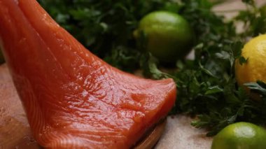Limon ve maydanozla çevrili tahta kesme tahtasına çiğ somon filetosunu gösteren videoyu kapat. Kaydırma kamera hareketi tazeliği ve dokuyu vurguluyor.