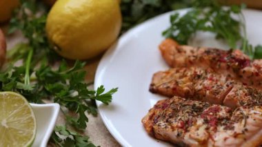 Maydanozlu somon filetosu, limon dilimleri, baharatlar ve ekmek çöreklerini beyaz tabakta gösteren bir sürgülü kamera videosu..