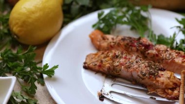 Maydanozlu, limonlu, baharatlı ve beyaz tabakta sunulan kızarmış somon filetolarını gösteren bir video..