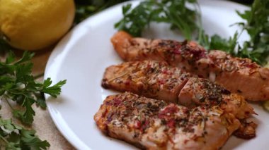 Maydanozlu kızarmış somon filetosu, limon dilimleri, baharatlar, ekmek çörekleri ve beyaz tabakta görünen limon suyunu gösteren bir video..