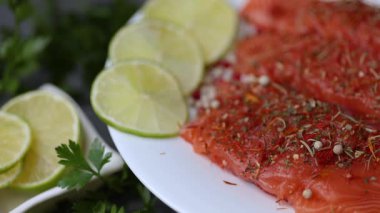 Maydanozlu somon filetosu, limon dilimleri ve beyaz tabakta sıralanmış baharatları gösteren bir video..