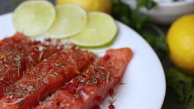 Maydanozlu somon filetosu, limon dilimleri ve baharatları beyaz bir tabakta gösteren kusursuz bir döngü videosu..