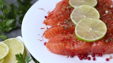 Maydanoz, limon dilimleri, limon dilimleri ve beyaz tabakta baharatlarla sıralanmış somon parçalarını gösteren dönen bir video..