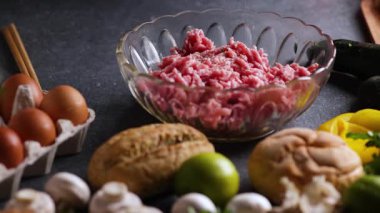 Mantar, limon, maydanoz ve yumurtalarla çevrili kristal bir kasede kıyma üzerine baharat serpiştiren bir şefin sürgülü kamera videosu..