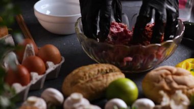 Şefin ellerini mantarlar, limonlar, çörekler, maydanozlar ve yumurtalarla kaplı kristal bir kasede kıyma yaparken gösteren sürgülü kamera videosu..