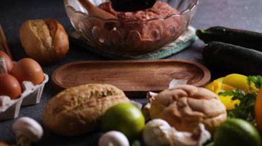 Bir köfte oluşturan bir aşçıyı gösteren ve limon, çörek, maydanoz ve yumurtalarla çevrili ahşap bir tabağa yerleştiren sürgülü kamera videosu..