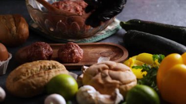 Birkaç köfte oluşturan ve onları limon, çörek, maydanoz ve yumurtanın yakınındaki ahşap bir tabağa yerleştiren bir şefin sürgülü kamera videosu..