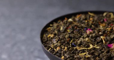 Tat veren yeşil çay yapraklarının eğik odak ile dönen makro videosu. Görünür gül yaprakları ve bitkiler bu doğal çay arka planına renk ve doku ekler..