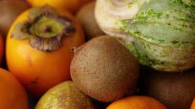 Mandalina armudu, kivi ve hurma içeren çizgili bir balkabağına odaklanan kayan bir video renkli mevsimlik meyve kompozisyonu oluşturuyor..