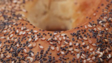 Tohumlu bagel çöreği ayrıntılı makro görünümde döner ve basit bir masa üstü sahnesinde kusursuz bir döngü olarak sunulur.