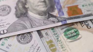 Üst üste binen katmanlara yerleştirilmiş 100 dolarlık banknotların, kabartmalı elementlerin, yazdırılmış yüzeylerin ve dikişsiz bir döngüdeki kağıt dokuların dönüşümlü makro görüntüsü..